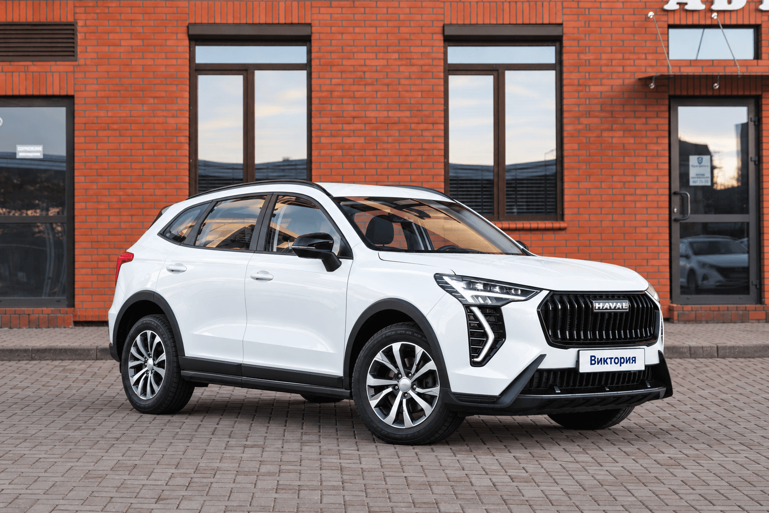 Белый Haval Jolion у офиса парка, передняя часть направлена вправо, на номере написано Виктория